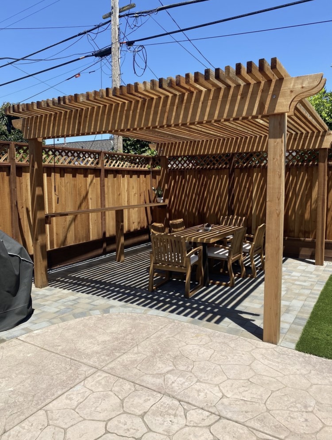 Outdoor patio with stamped concrete and pavers. An outdoor table and chairs sitting underneath a pergola.